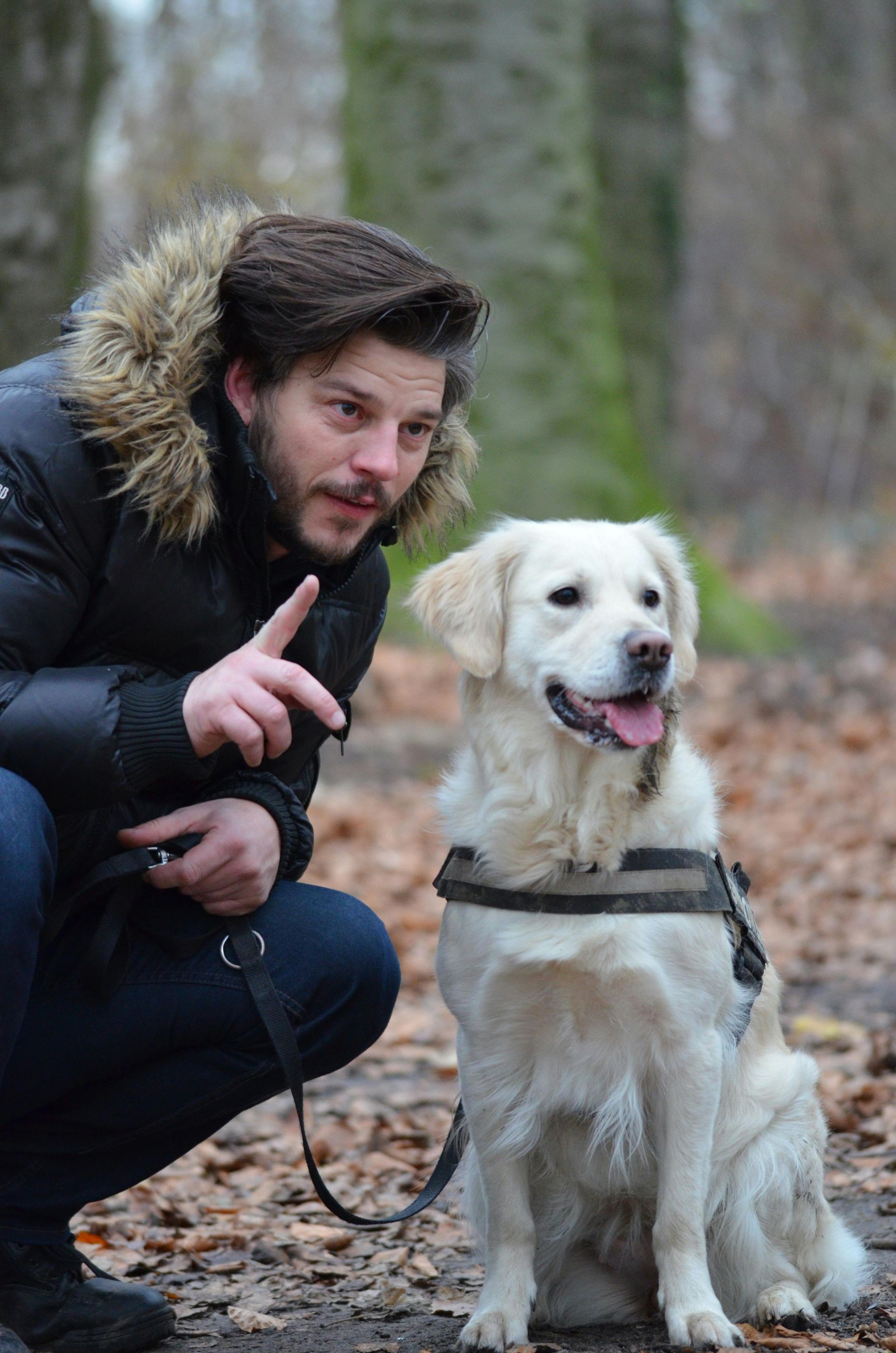 A man is kneeling down next to a dog in the woods.