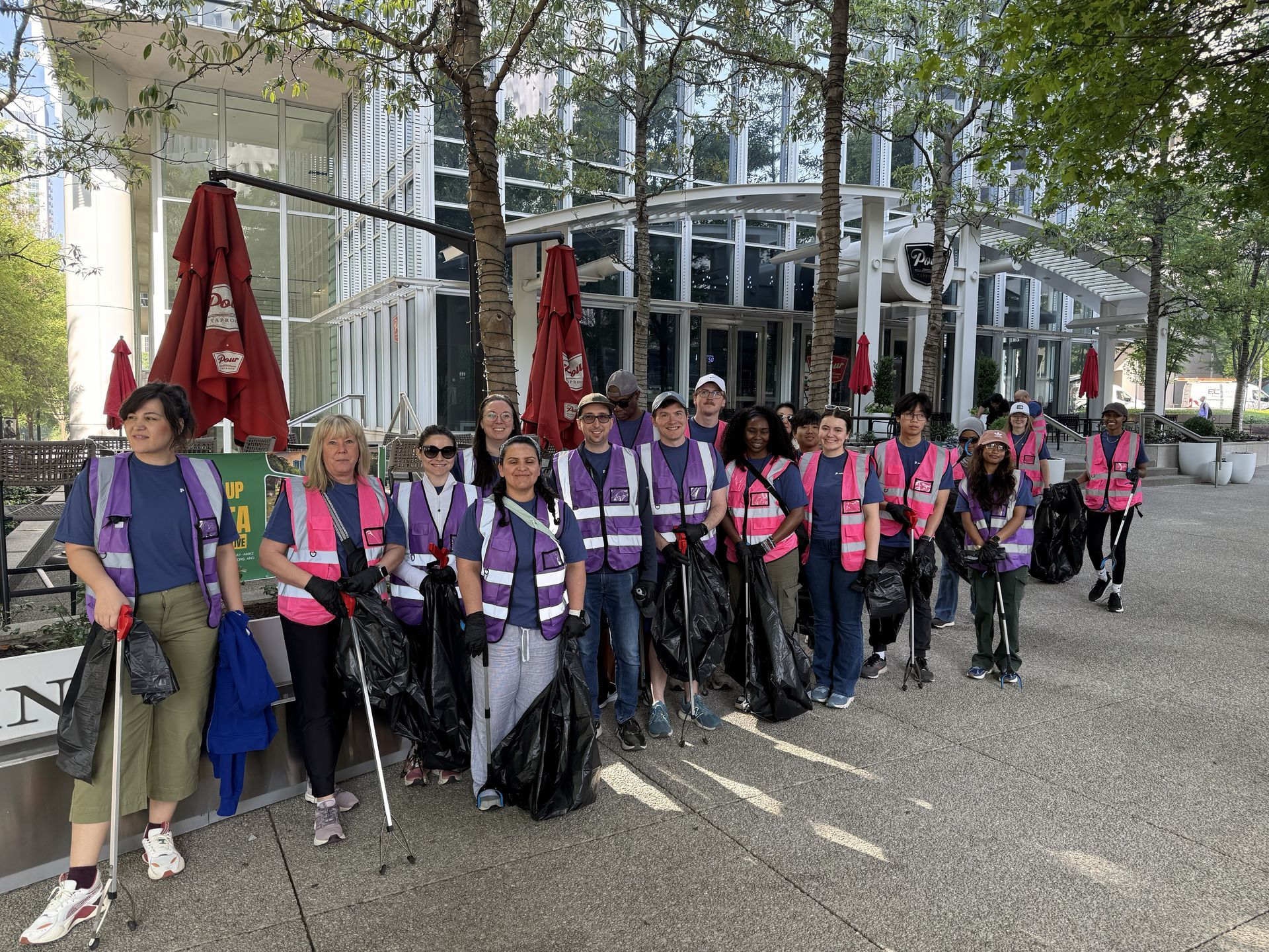 Group of people in purple and pink safety vests holding white canes on a city sidewalk near a glass building