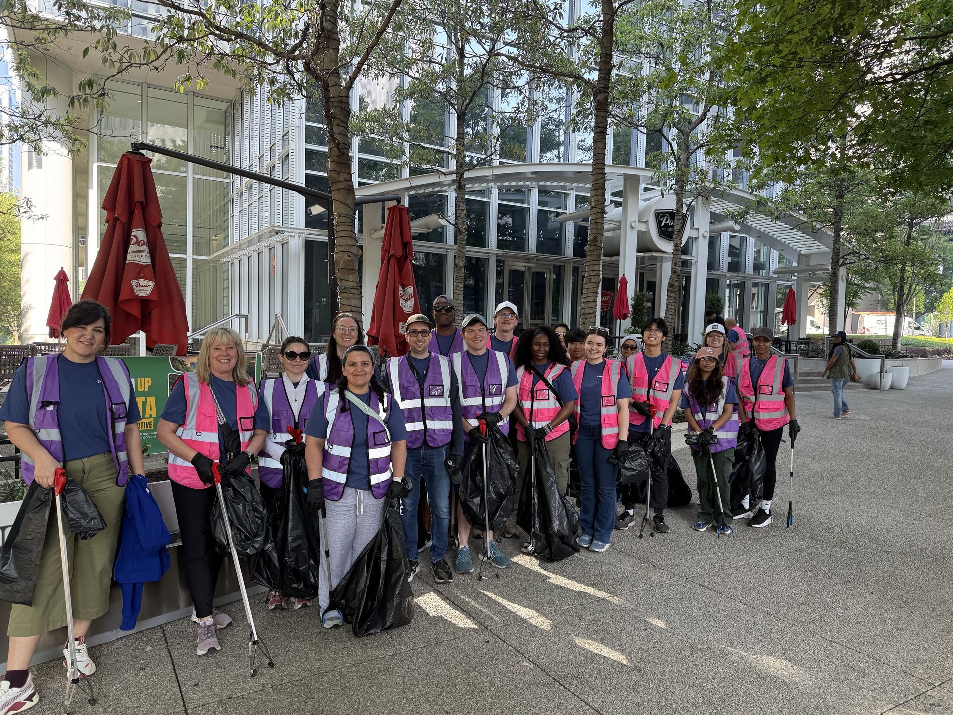 Group of volunteers in pink vests standing with hiking poles outside a glass building