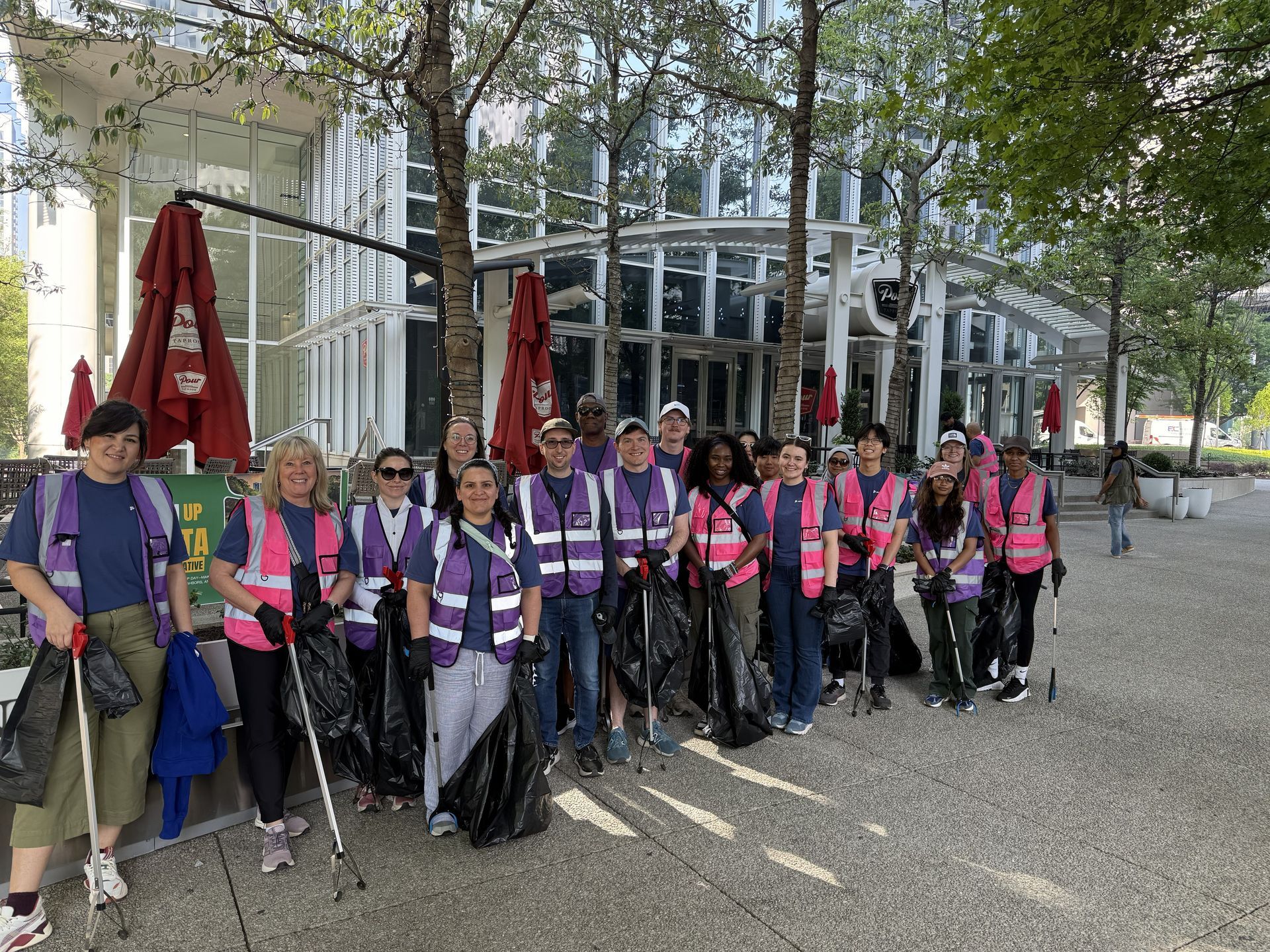 Group of people in pink vests and helmets posing with trekking poles outdoors by a glass building.