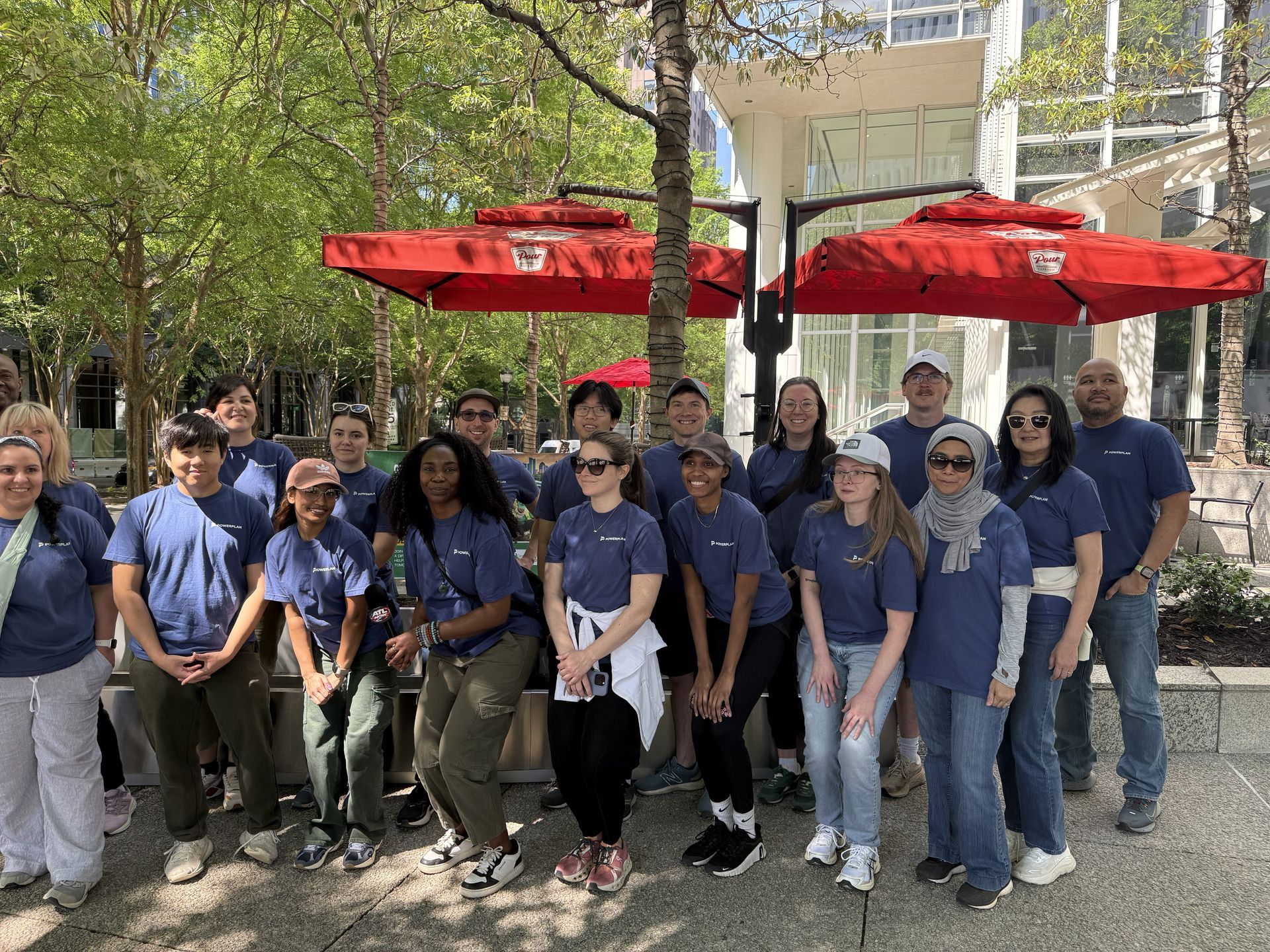 Group of people in blue shirts posing outdoors under red umbrellas in a park-like setting