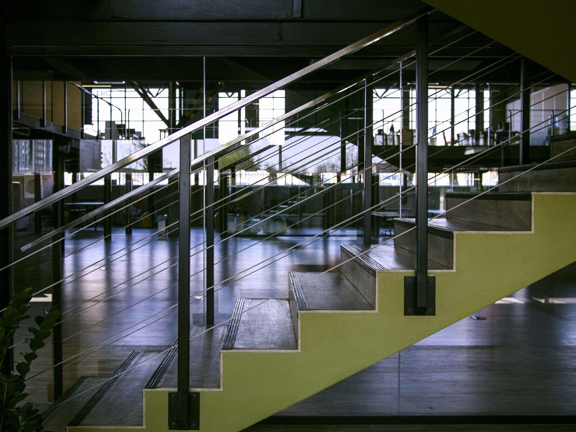 Staircase with lime green side and dark metal railing, leading to an open office space with large windows.