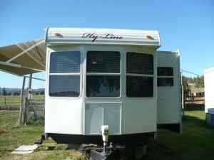 A white trailer is parked in a grassy field under a canopy.