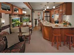 A living room and kitchen in a rv with wooden cabinets and stools.