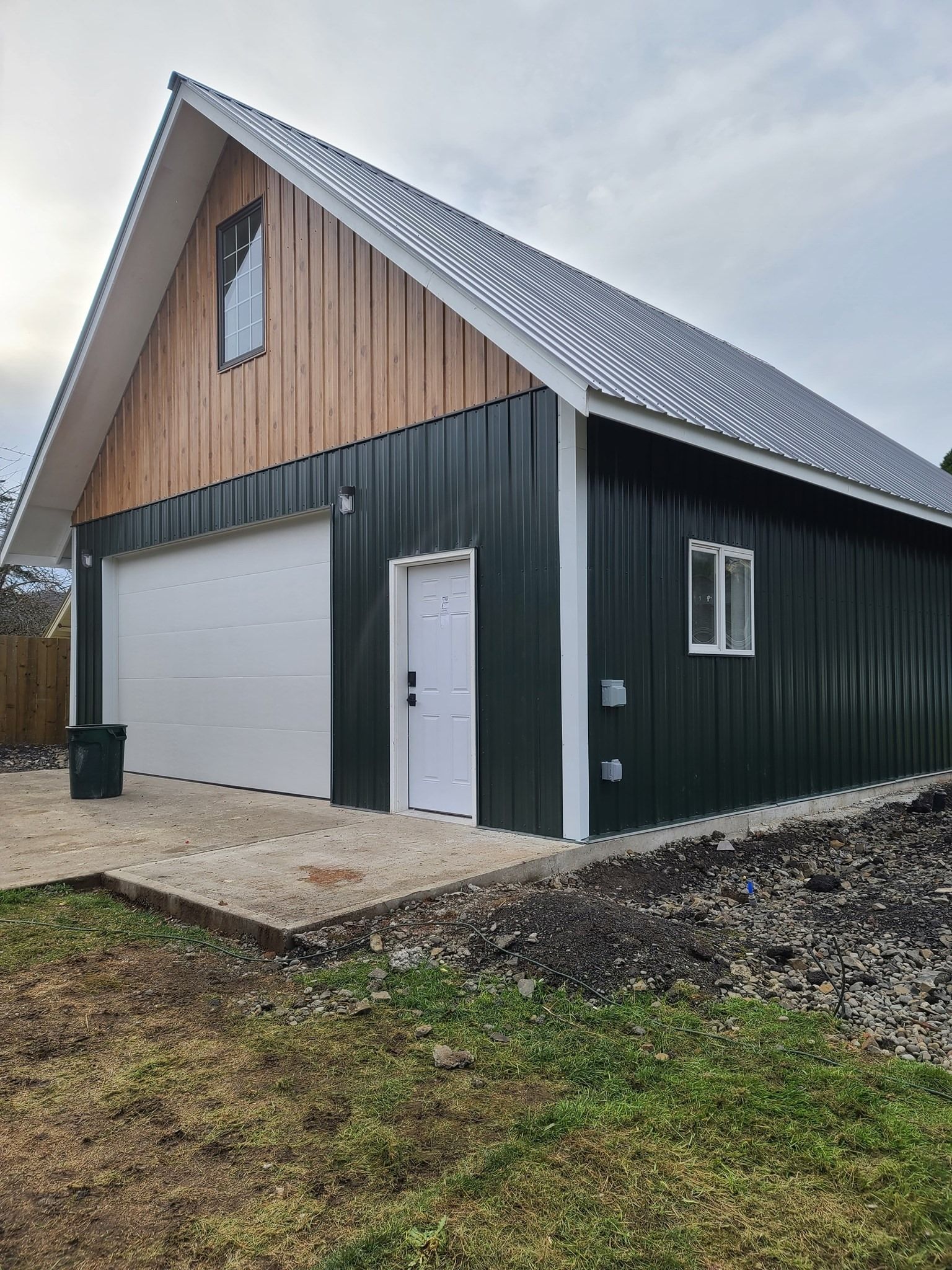 A house under construction with a new roof and porch, surrounded by gravel and trees.