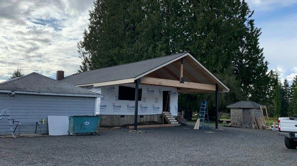 A house under construction with a new roof and porch, surrounded by gravel and trees.