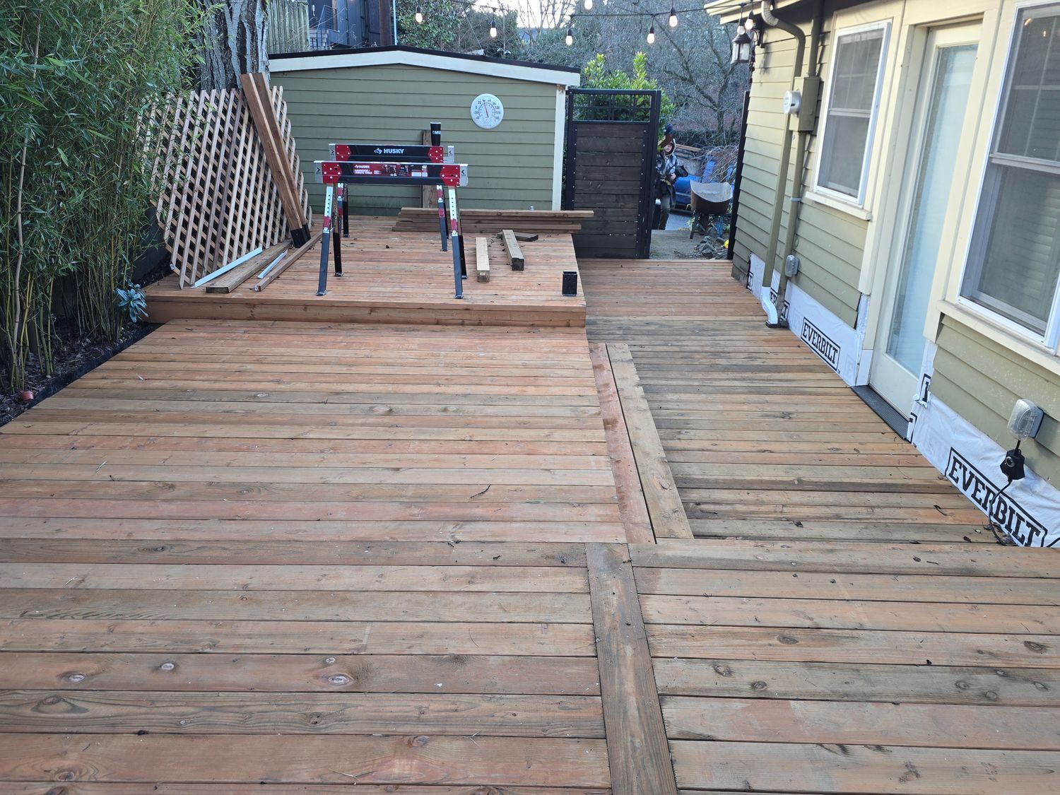 Wooden deck construction in progress next to a yellow house with a shed in the background.