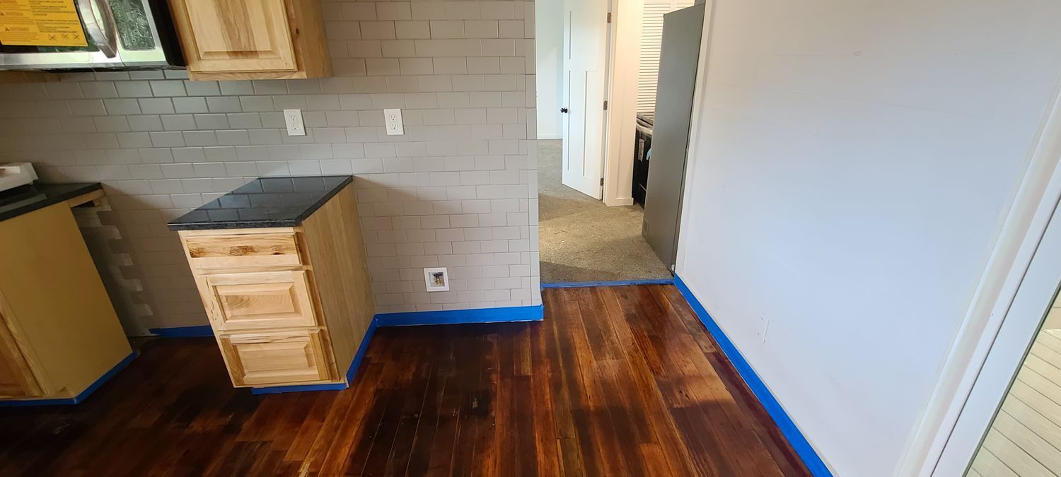 Kitchen with wooden cabinets, brick backsplash, and hardwood floors. Blue tape protects the edges.