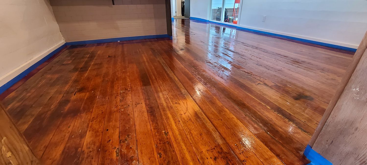 Wooden floor with wet finish, protected by blue painter's tape along the walls.