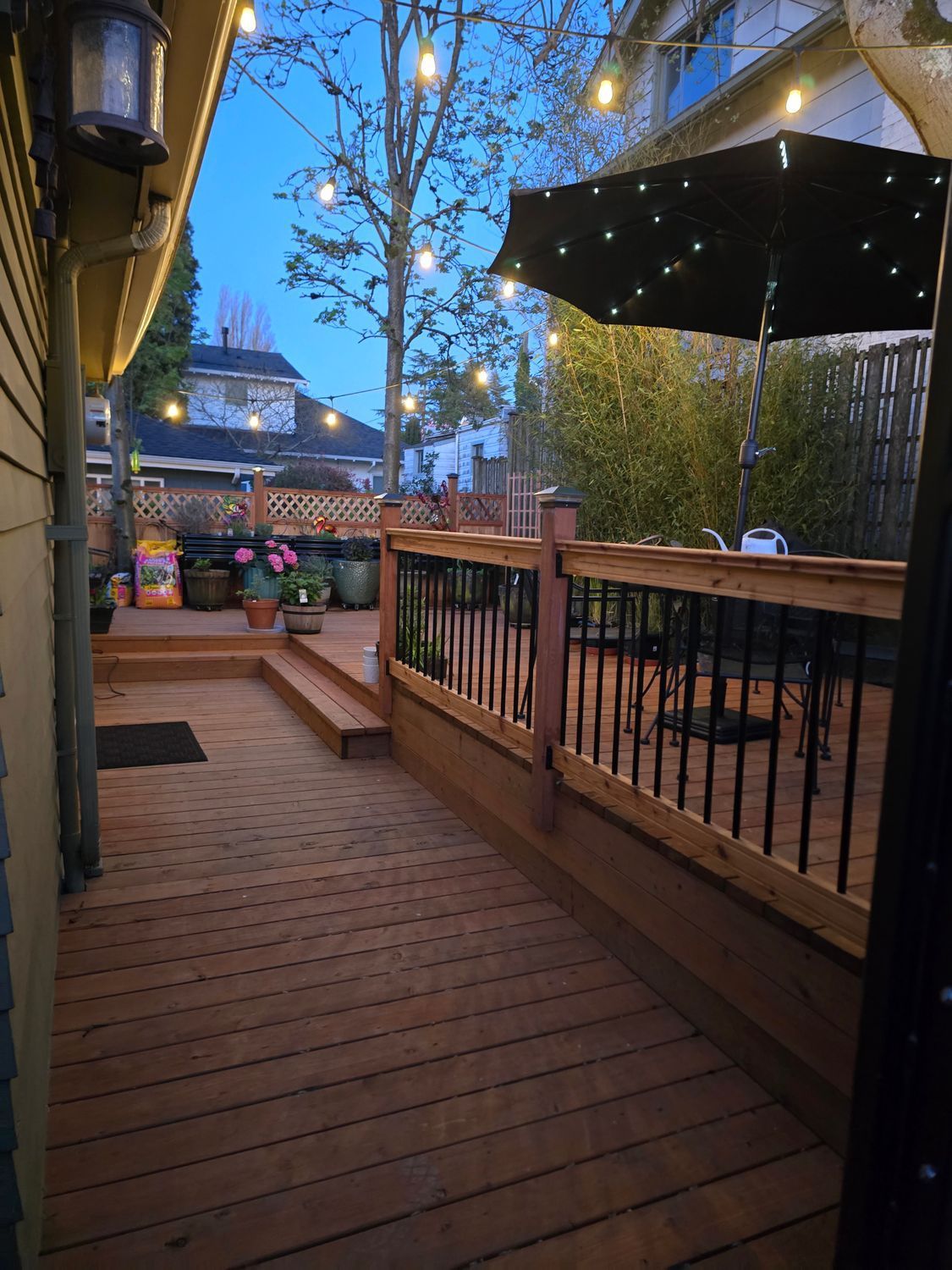 Wooden deck at dusk with string lights and an umbrella.