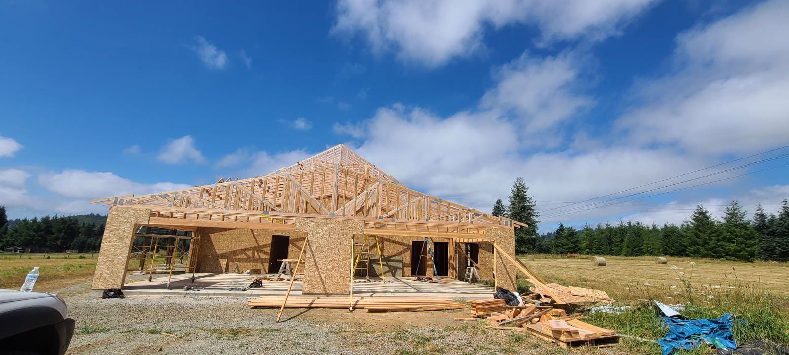 Wooden deck with pergola, table, and bench, bathed in sunlight. Green trees and blue sky in background.