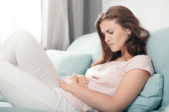 Young Woman in Pain Lying on Couch at Home — Louisville, KY — Kentuckiana Gastroenterology & Paramount Surgery Center