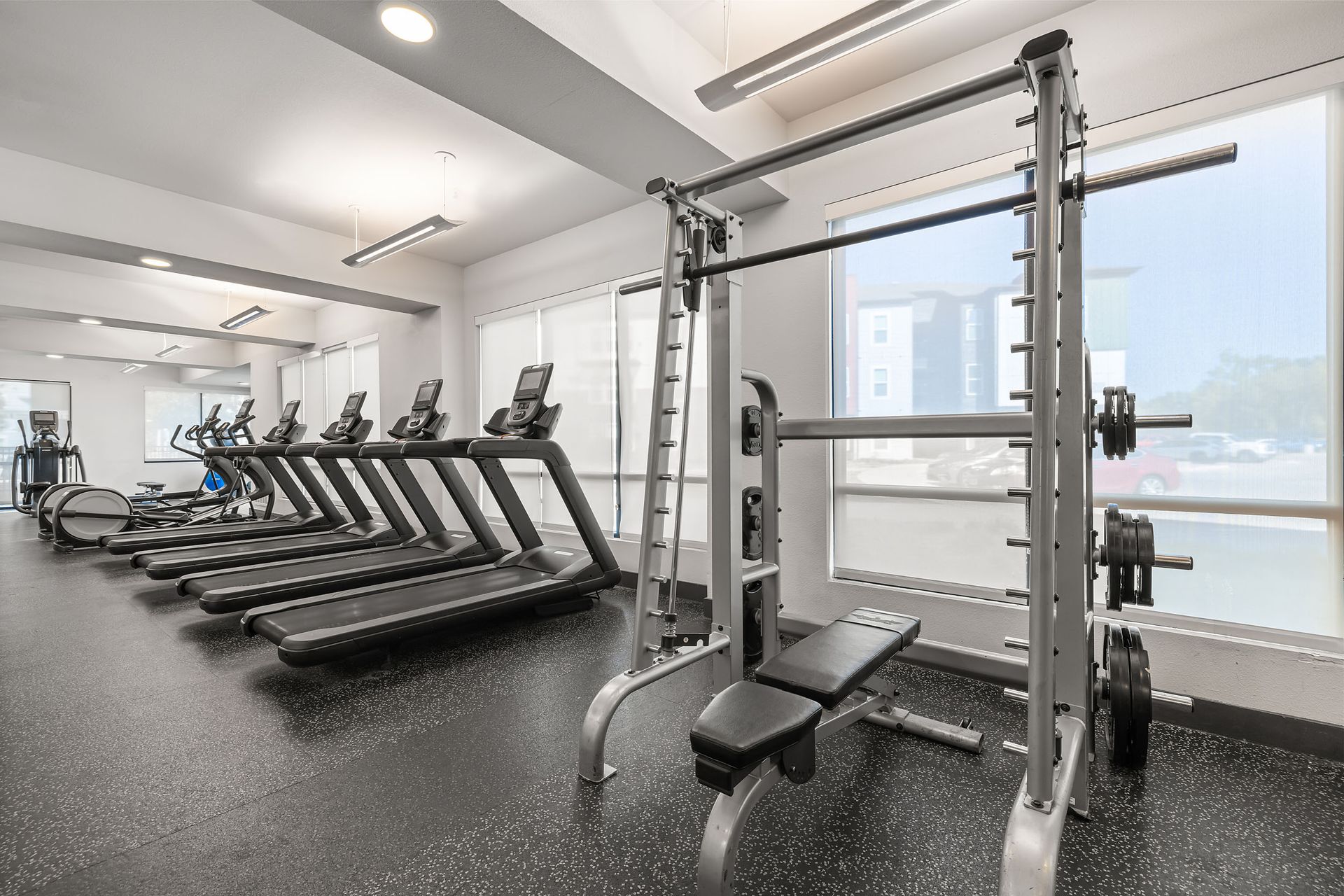 A gym with treadmills, a bench, and a barbell rack at The Heights offers student apartments for rent near SHSU.