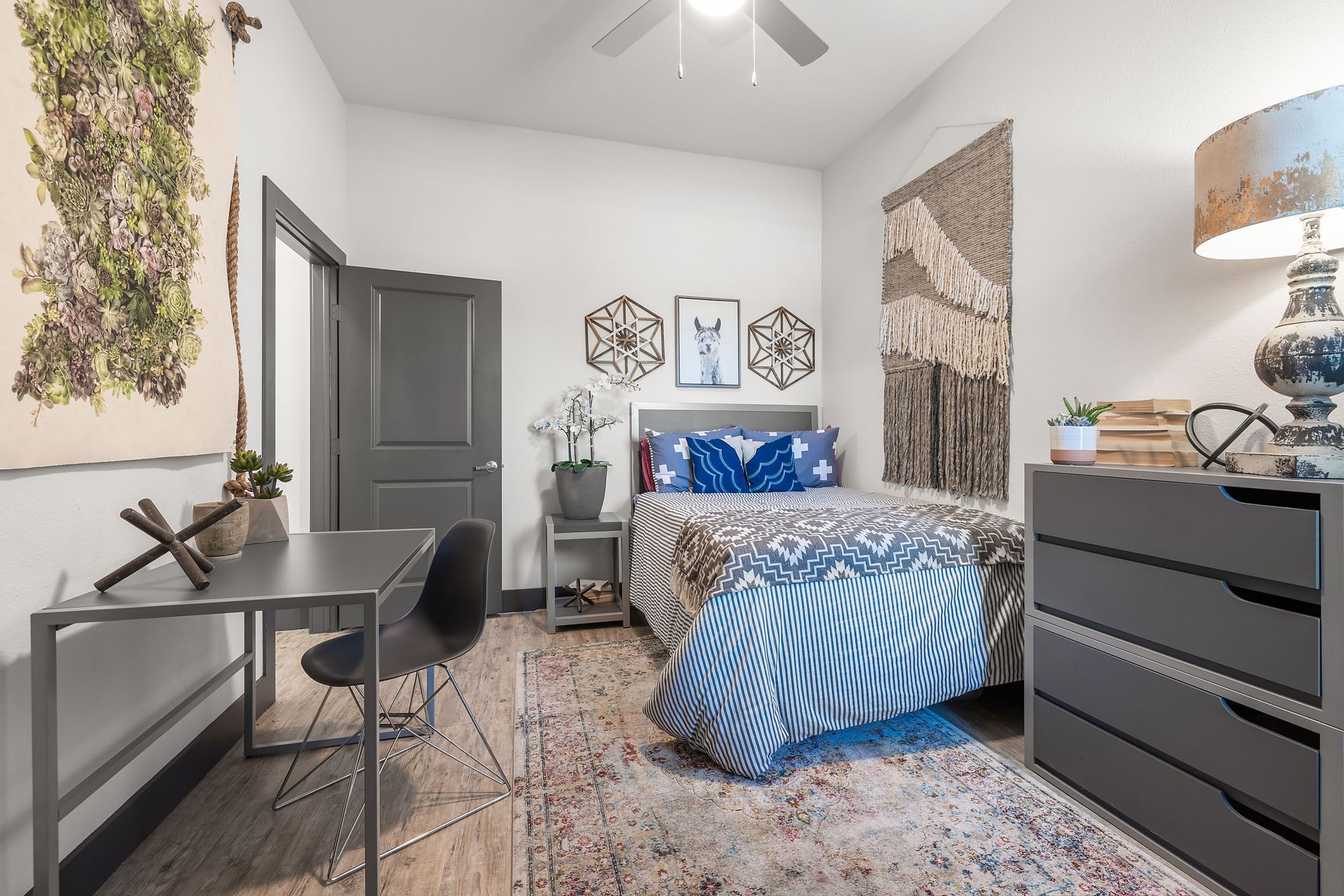 Apartment bedroom with a bed, desk, dresser, ceiling fan, and chair at The Heights offers student apartments for rent near SHSU in Huntsville, TX.