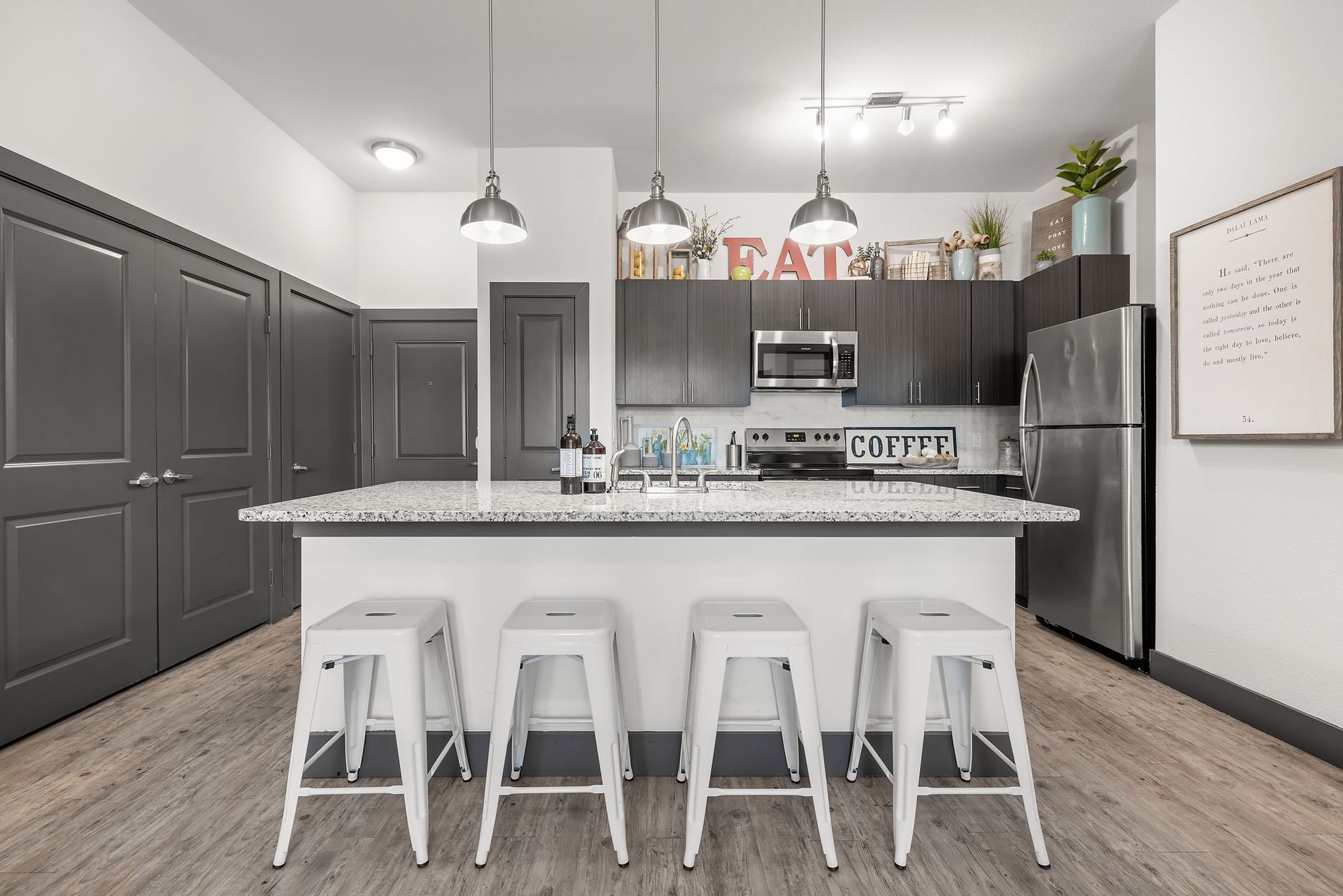 Modern kitchen with a large island, 4 bar stools, and dark grey cabinets at The Heights offers student apartments for rent near SHSU in Huntsville, TX.