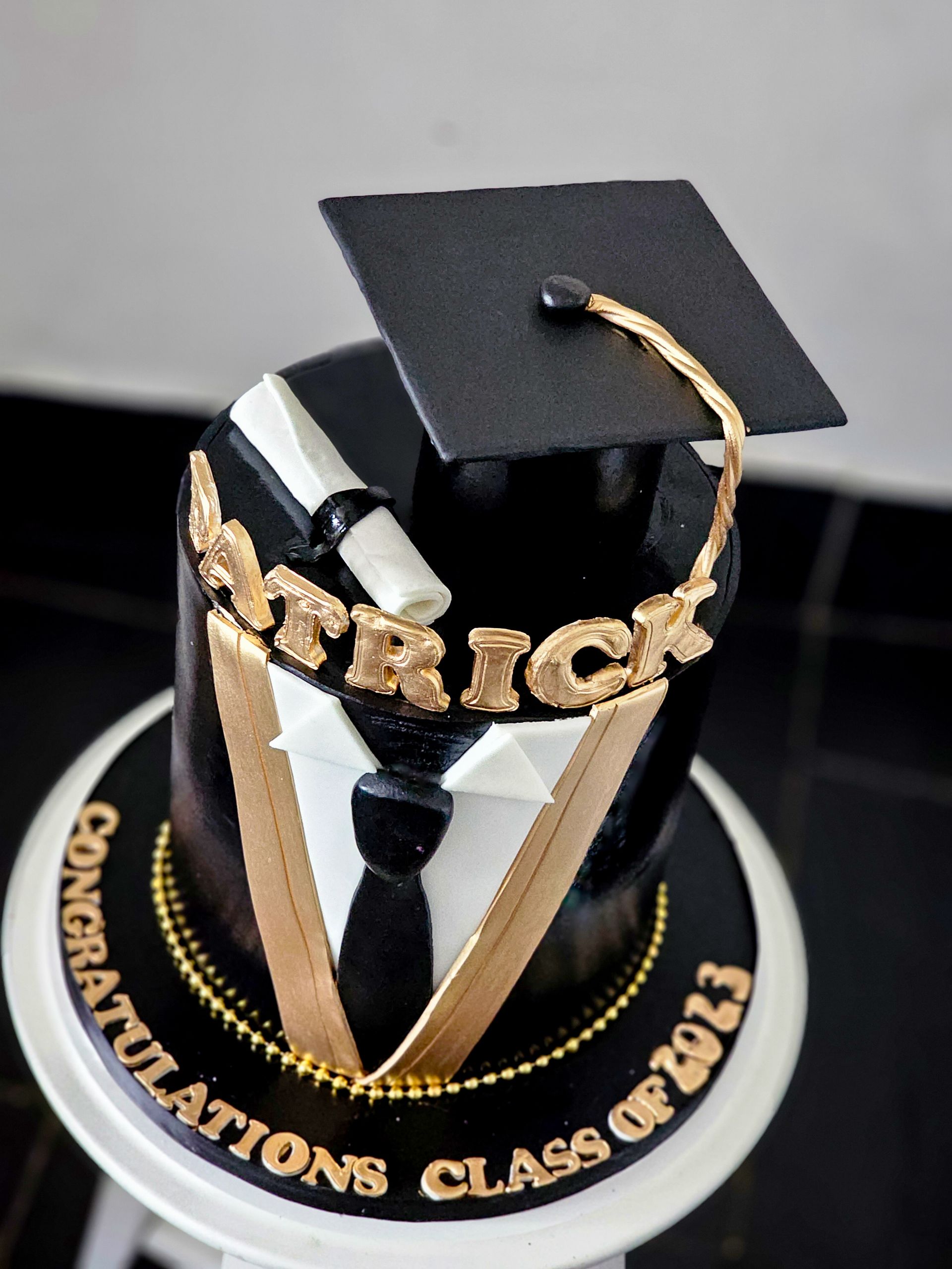 Graduation cake decorated as a black suit with a mortarboard, diploma, and gold lettering that says 