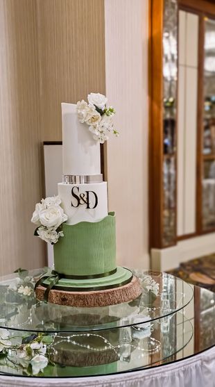 Three-tiered wedding cake with white and green tiers, initials, and floral decorations