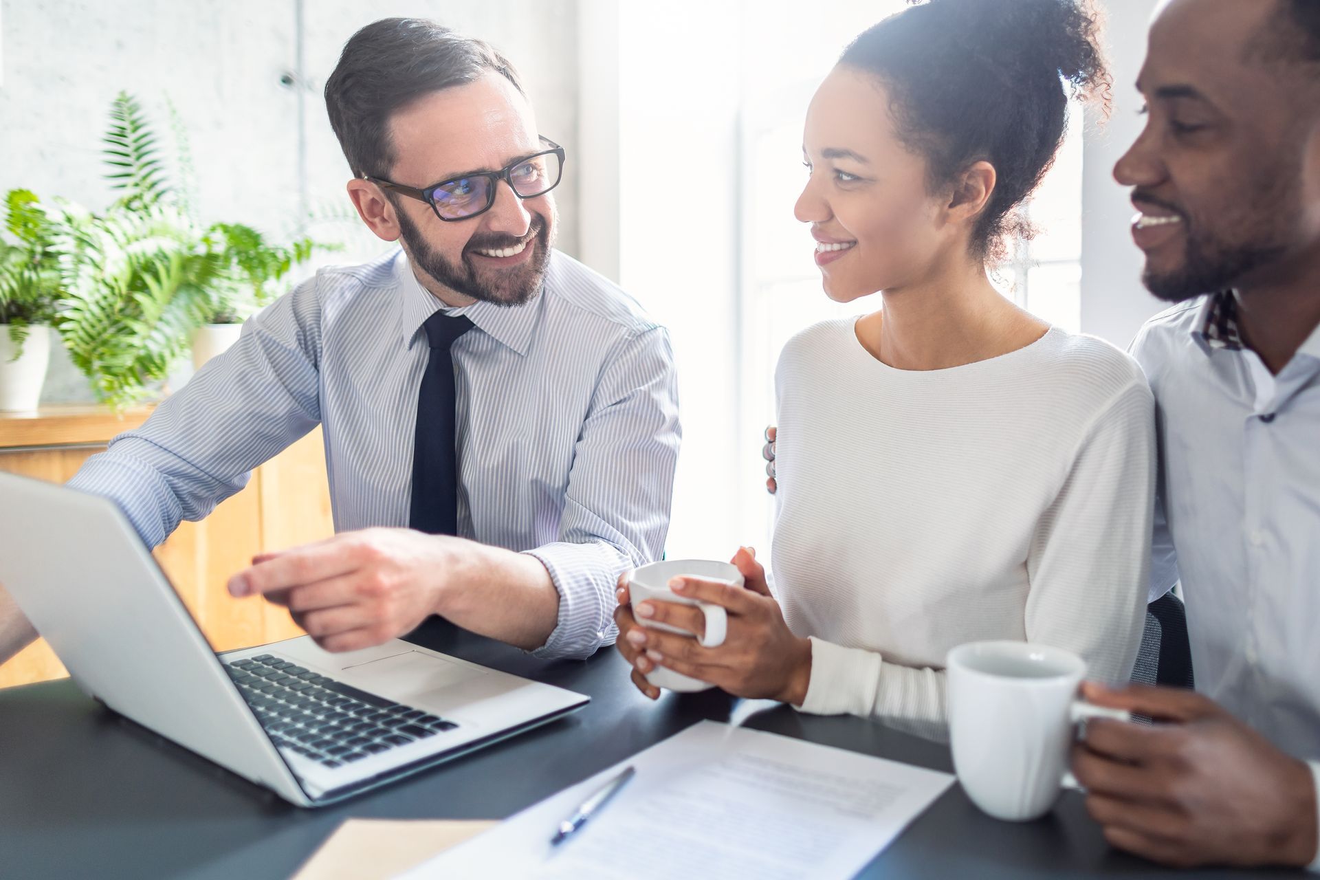 A man and a woman are sitting at a table looking at a laptop.