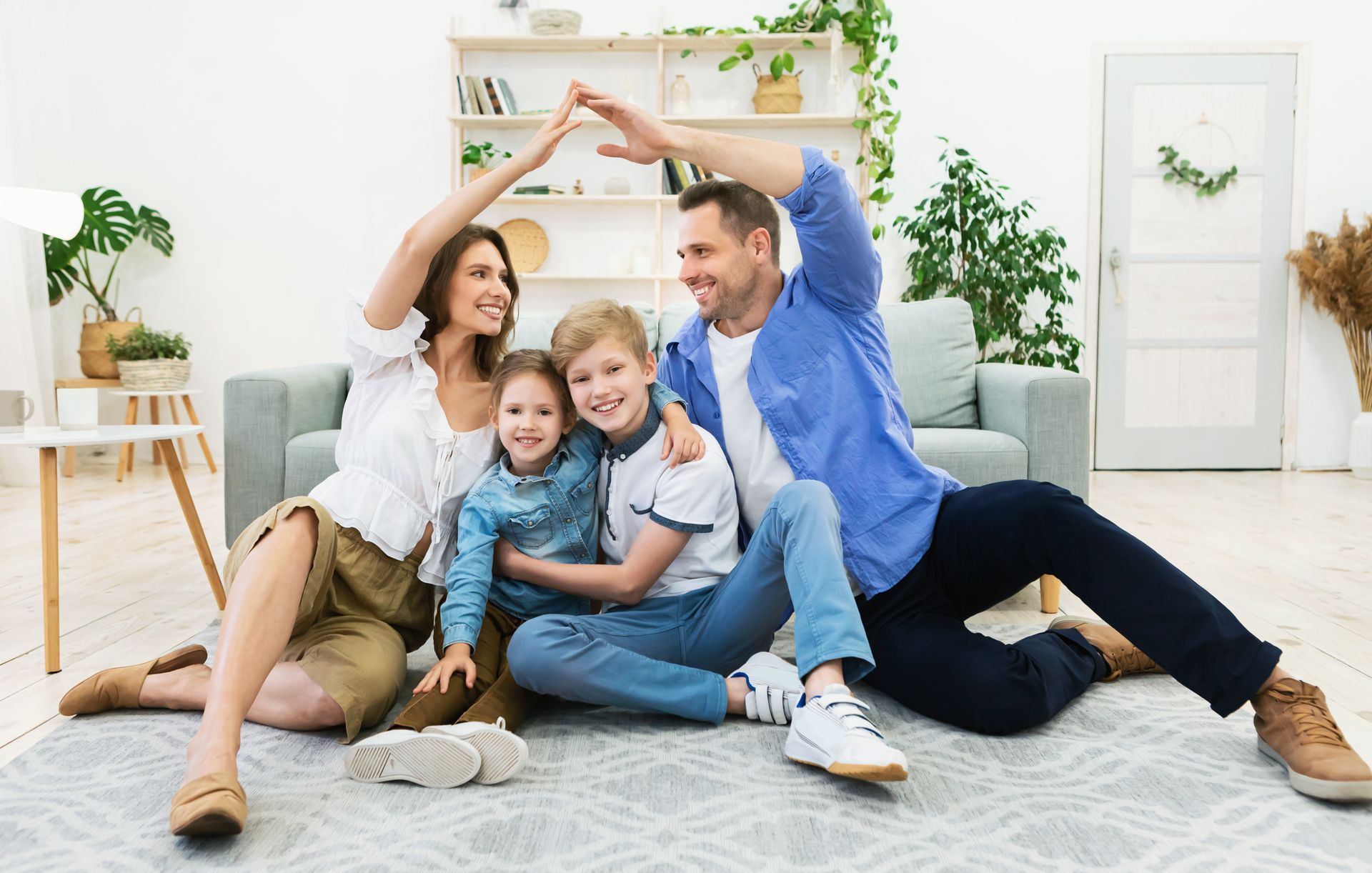 A family is sitting on the floor in a living room making a house with their hands.