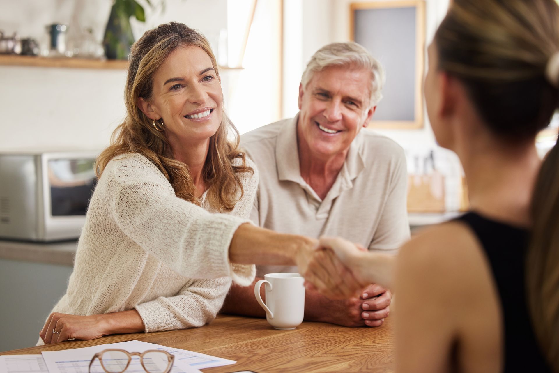 A woman is shaking hands with a man and woman while sitting at a table.
