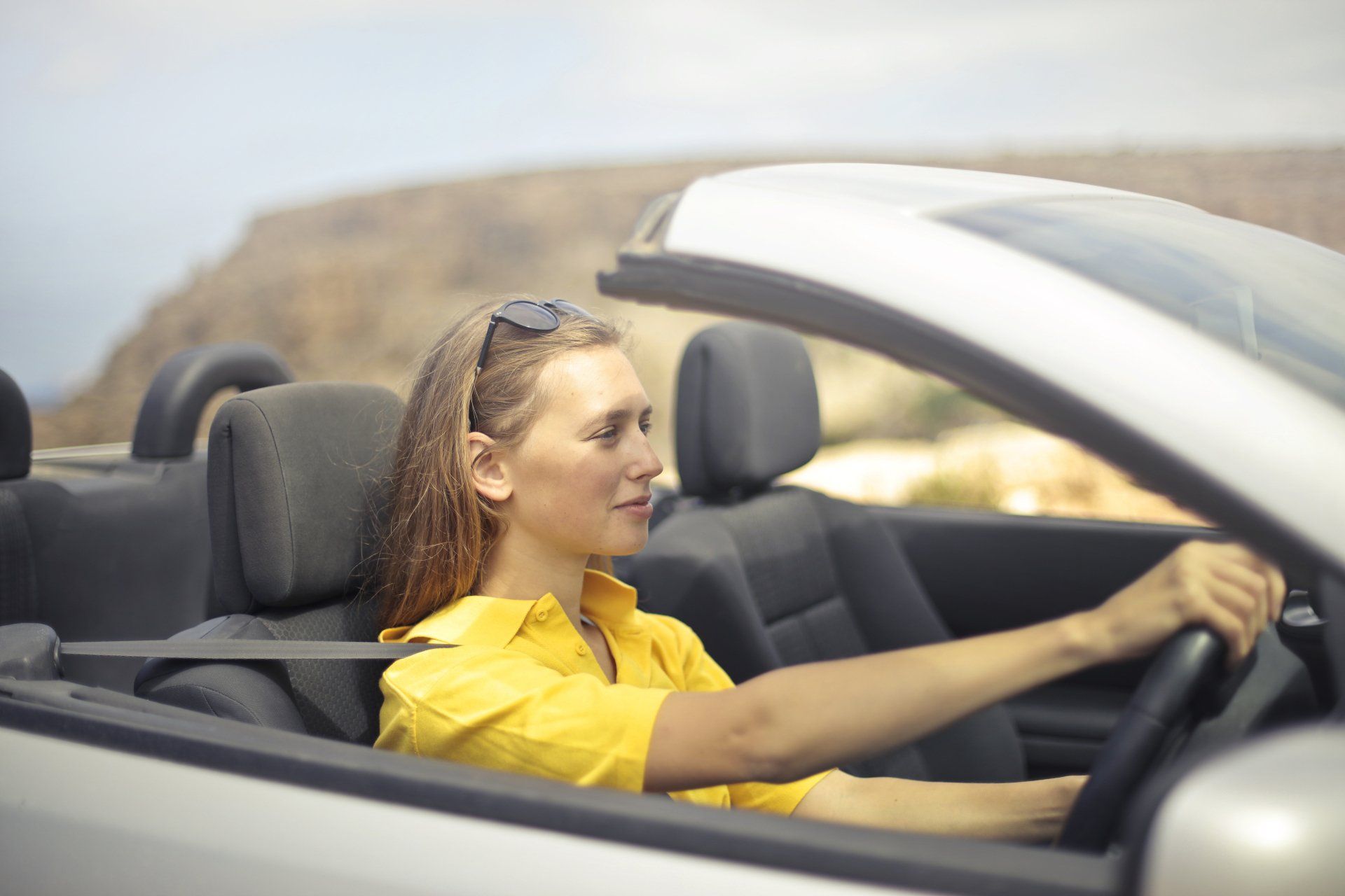 A woman in a yellow shirt is driving a convertible car.