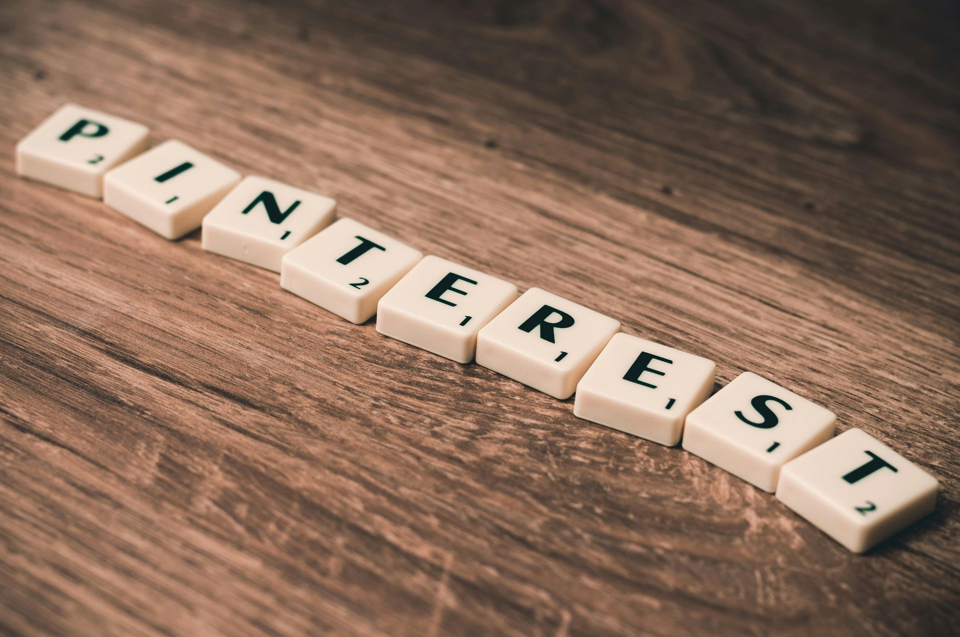 The word Pinterest is written in scrabble tiles on a wooden table.