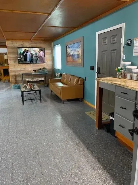 Living room with tan couch, turquoise wall, and TV. Gray speckled floor.