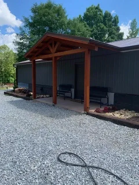 Brown wooden porch over a gray building with two benches, set on gravel.