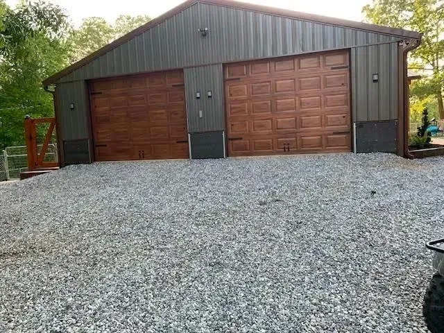 Two-car garage with brown doors and gray metal siding. Gravel driveway leads up to the structure.