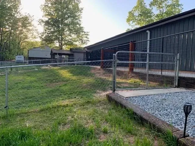 Chain link fence surrounds a grassy yard and a building with red and grey exterior.