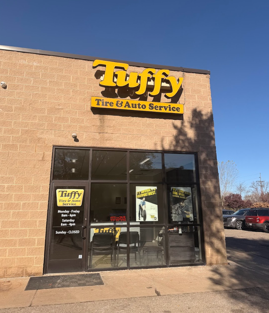Tuffy Tire & Auto Service storefront with yellow sign on a brick building, glass door, and parked cars.