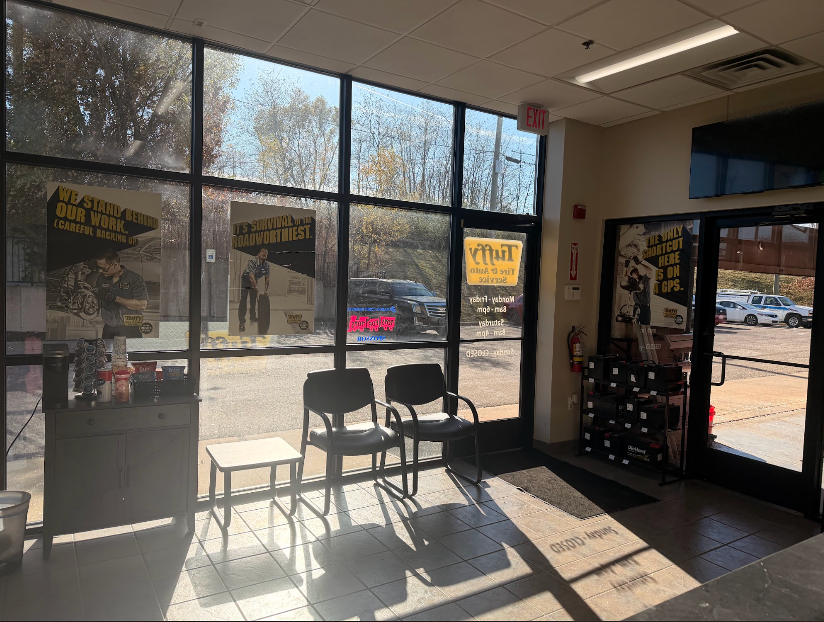 Interior of an auto shop waiting area with chairs, windows, and sunlight. A car is visible outside.