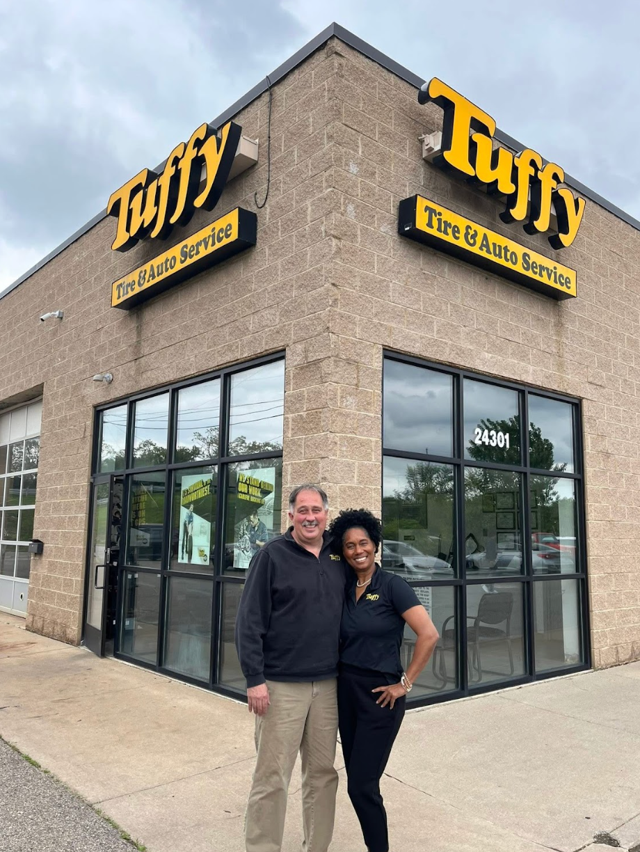 Two people stand outside Tuffy Tire & Auto Service. Building is tan brick.