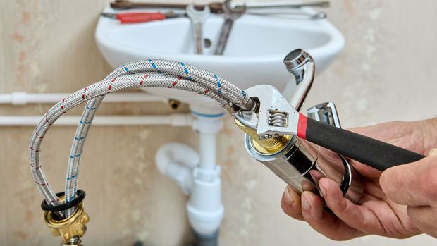 Man applying drywall mud to wall, using a long metal trowel. Indoors, white wall and ceiling.