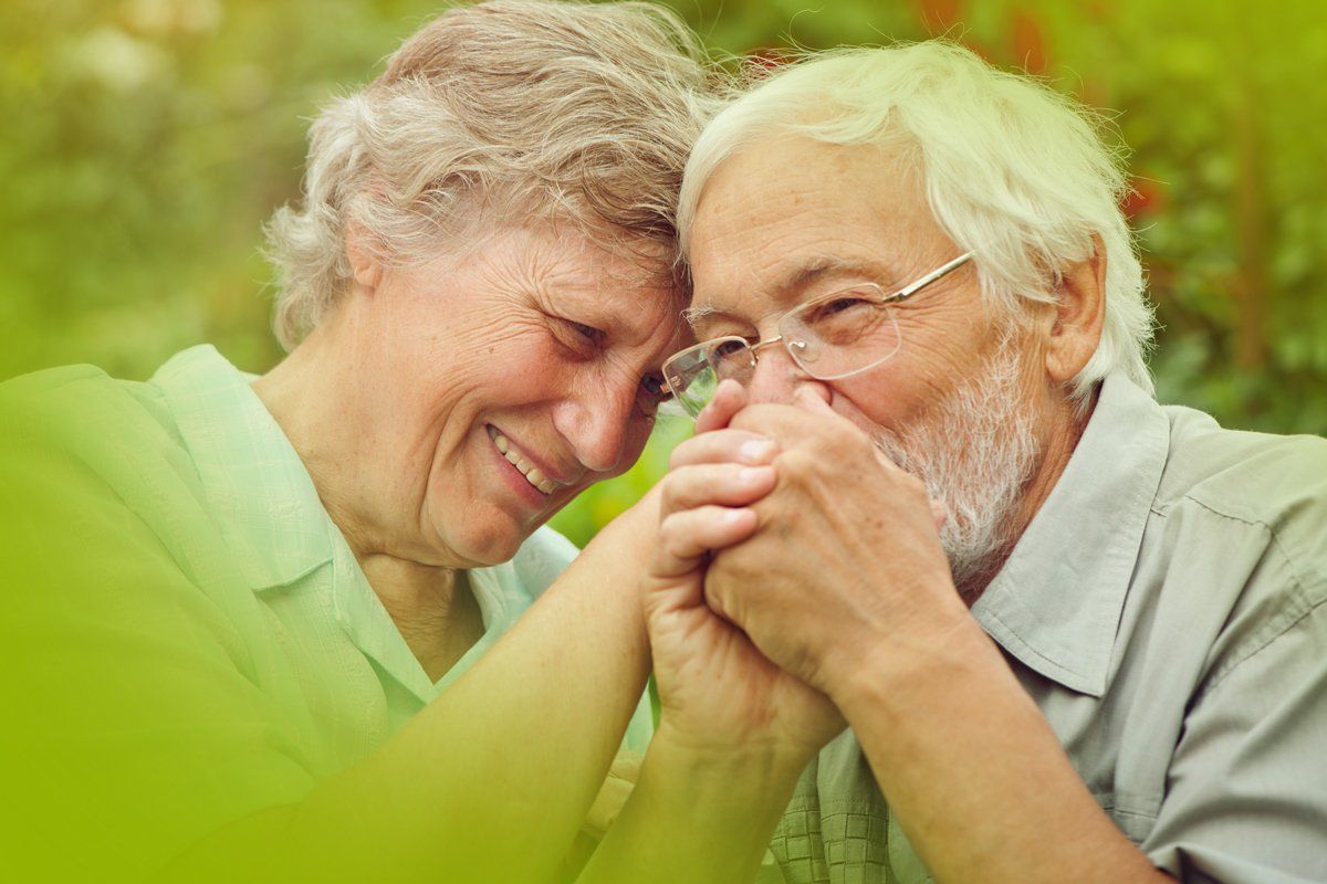 An elderly couple is holding hands and smiling.