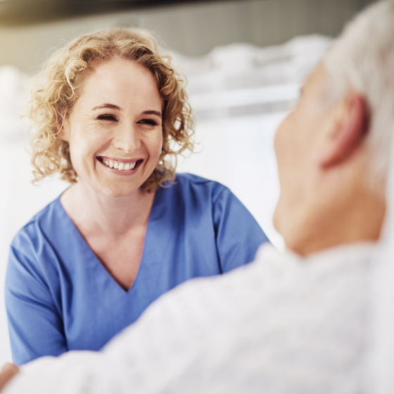 A nurse is smiling while talking to an elderly man.