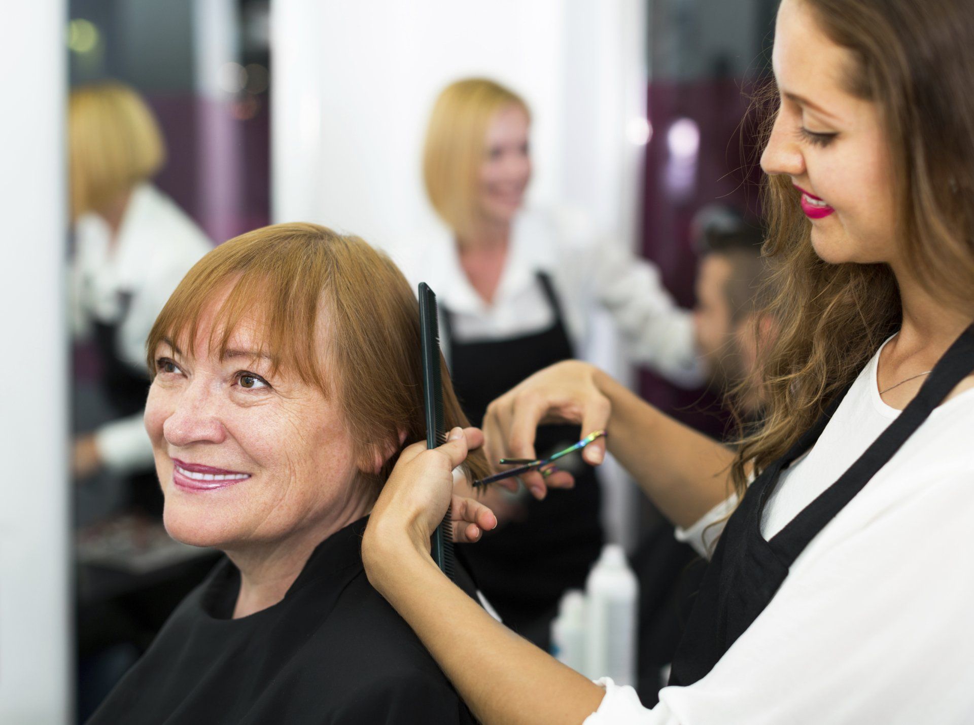A woman is getting her hair cut by a hairdresser in a salon.