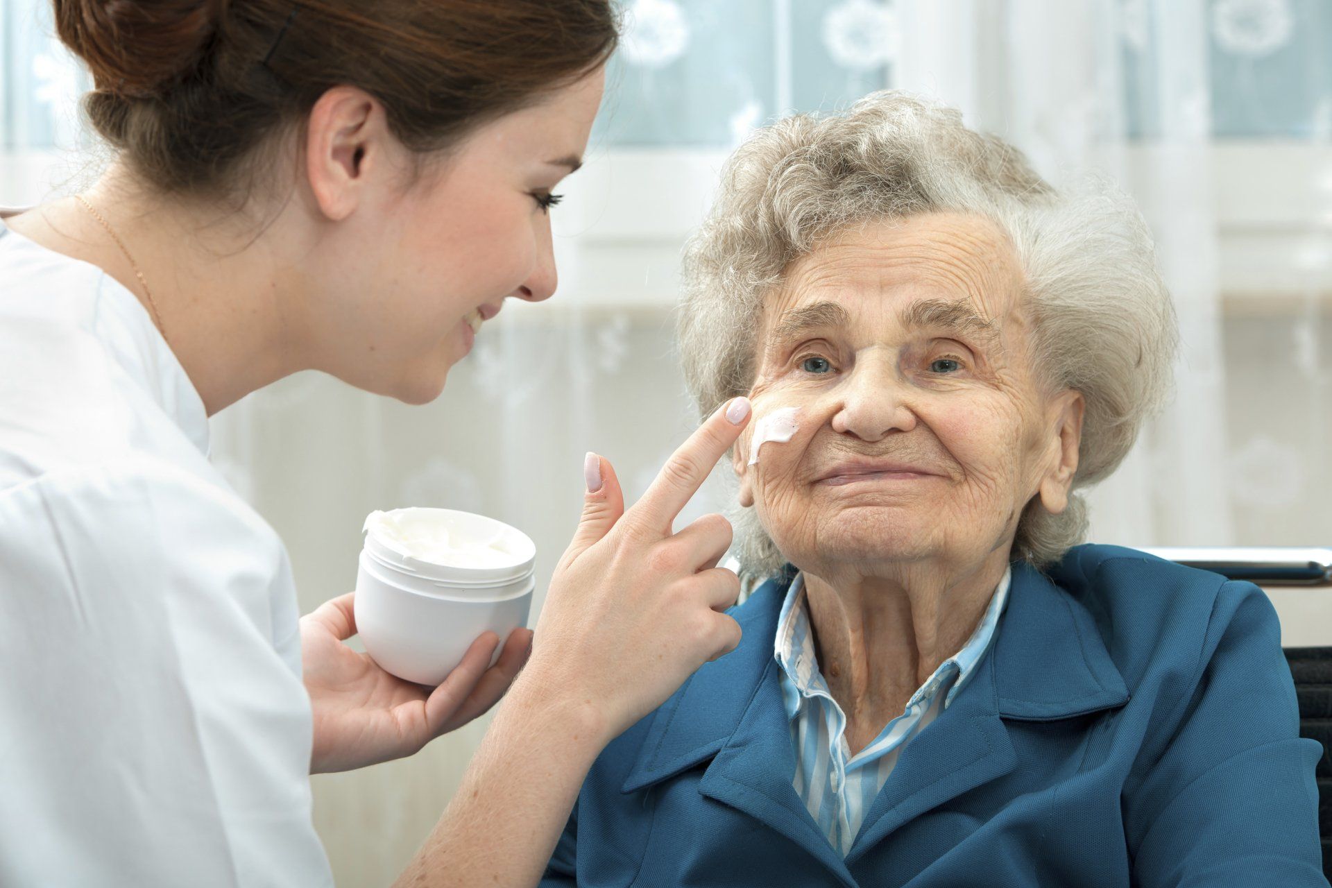A nurse is applying cream to an elderly woman 's face.