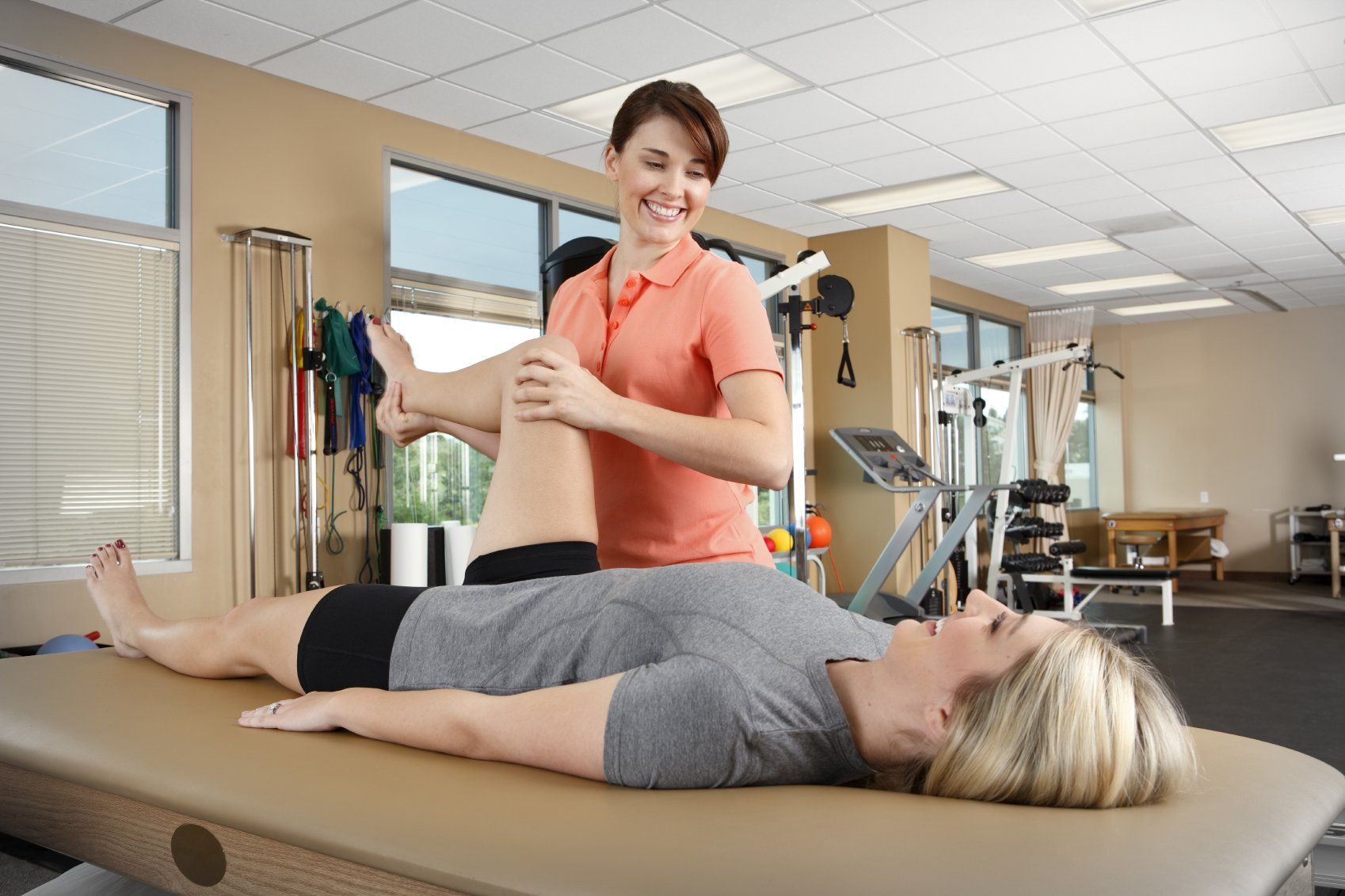 A woman is laying on a table getting her leg examined by a female physical therapist.
