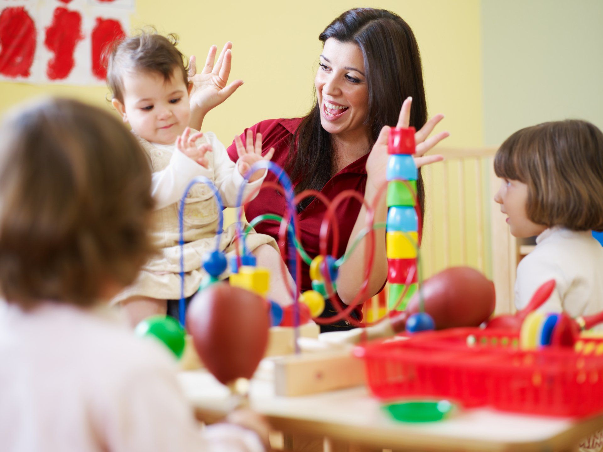 A woman is playing with a baby in a room with other children.