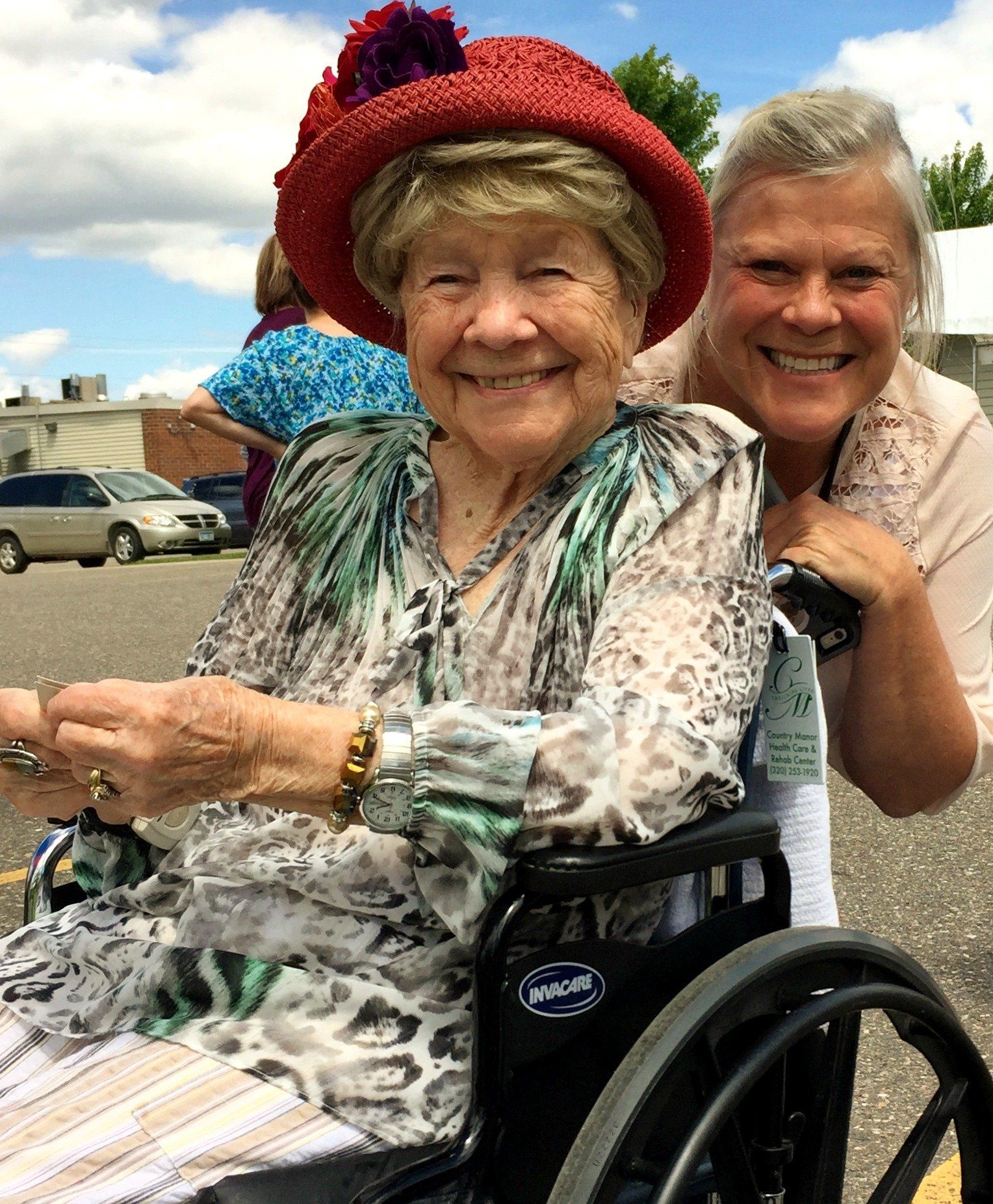 A woman in a wheelchair is being pushed by another woman wearing a red hat
