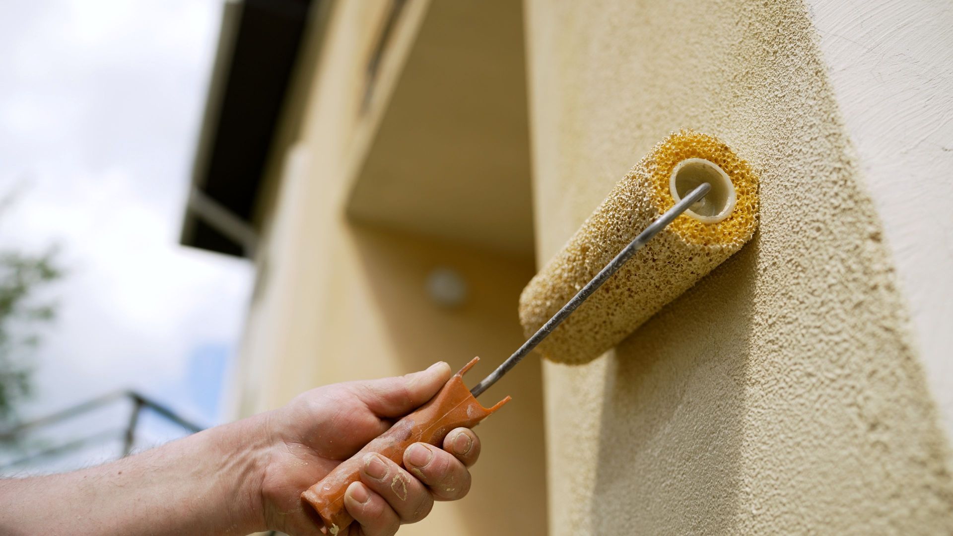 A medium shot of a wall painting as a painter uses a roller on a house exterior