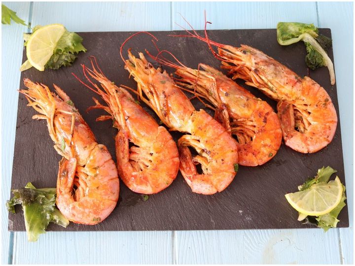 Cinque gamberi grigliati su un tagliere di ardesia scura, guarniti con spicchi di lime.