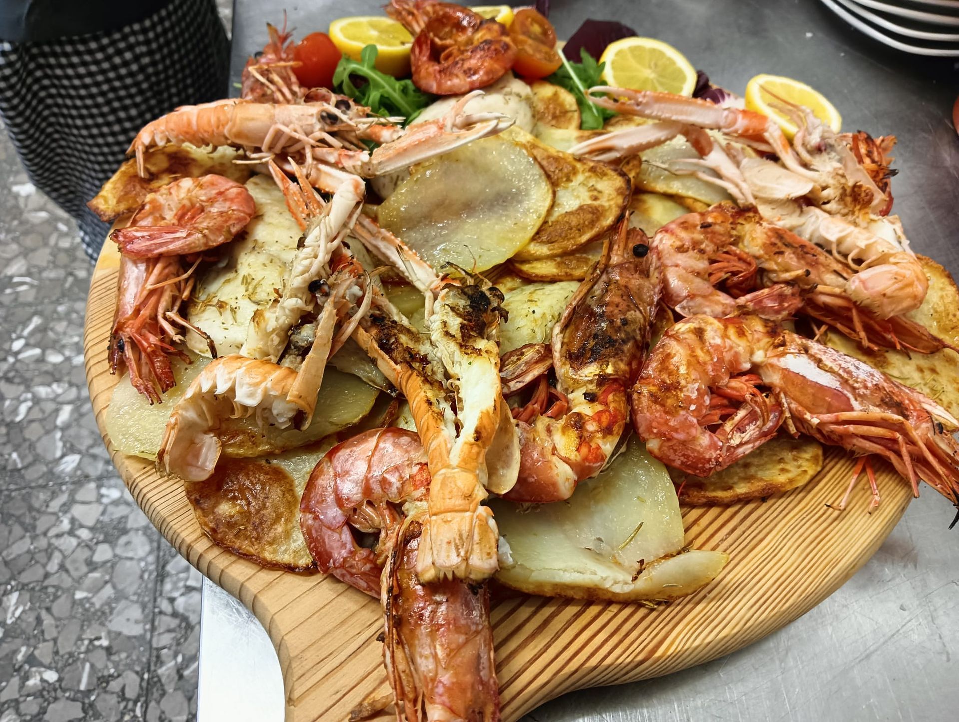 Piatto di frutti di mare con gamberi grigliati, zampe di granchio e spicchi di limone su un tagliere di legno.