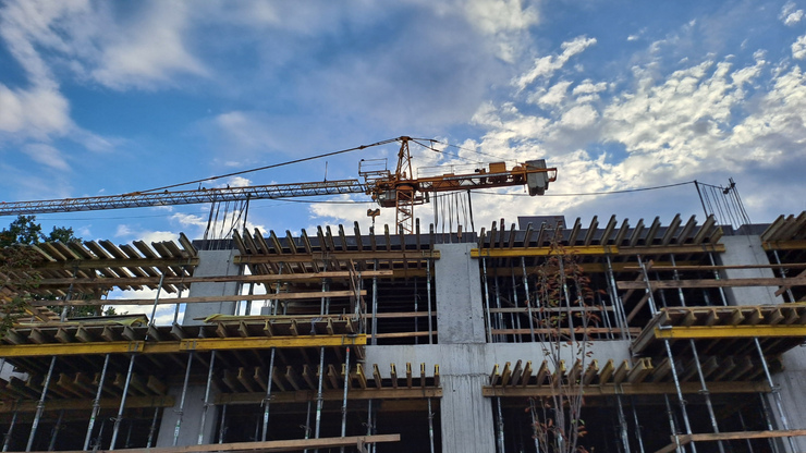 Construction site with a crane against a blue sky with clouds. Building has wooden frames.