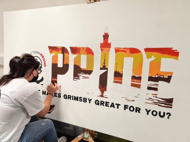 A woman is painting the word pride on a wall