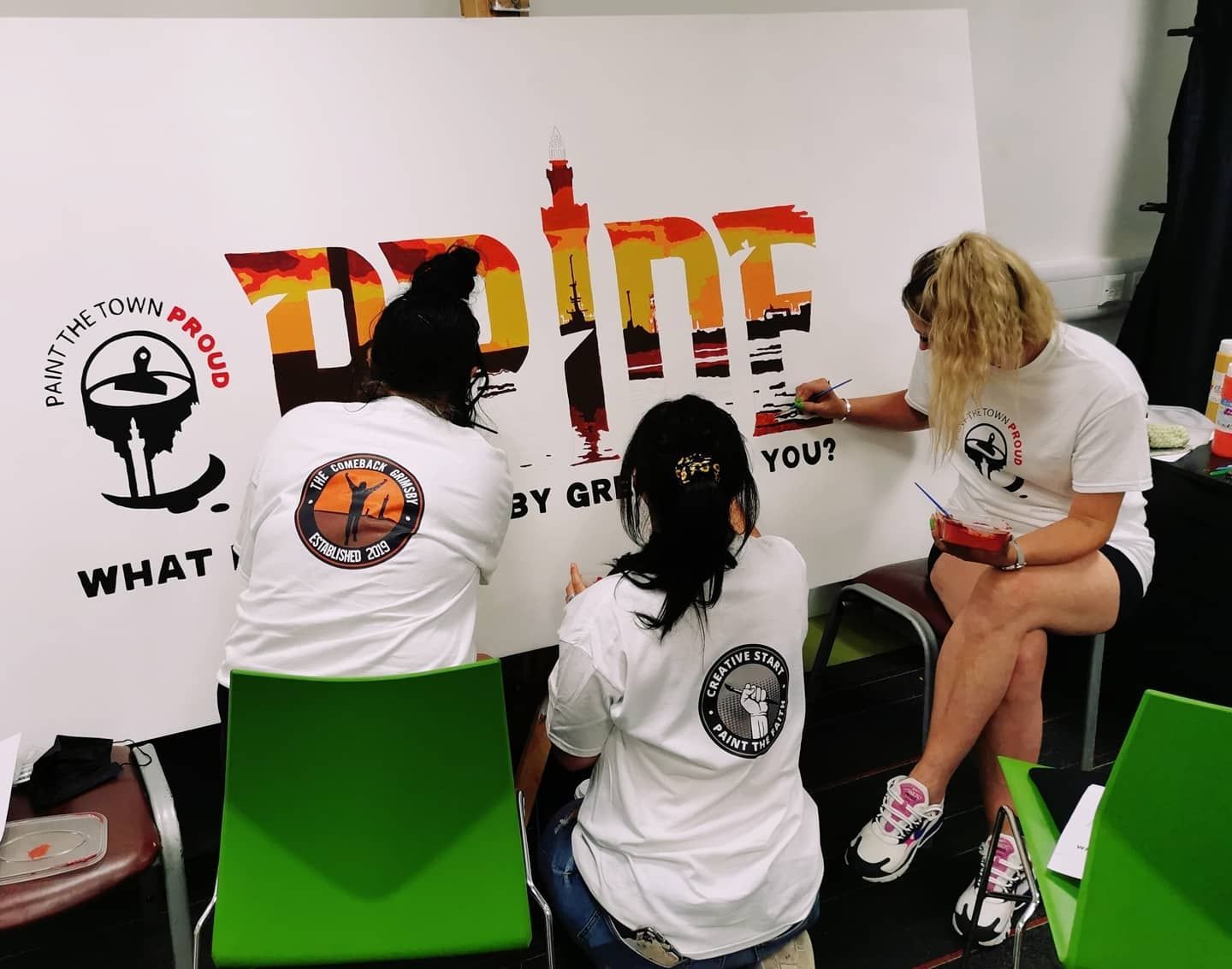 Three women are painting a large sign that says 