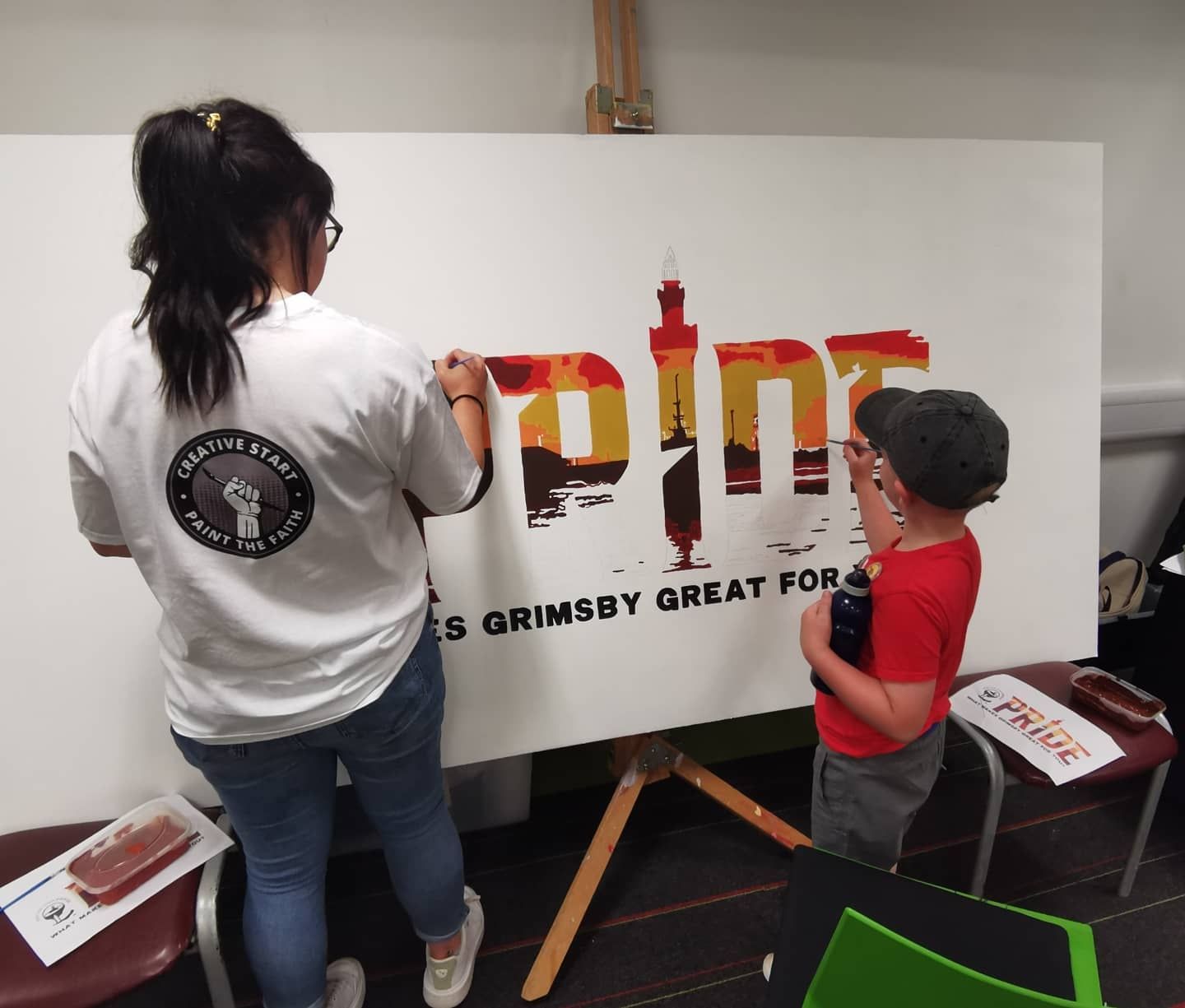 A girl and a boy are painting the word pain on a large white board