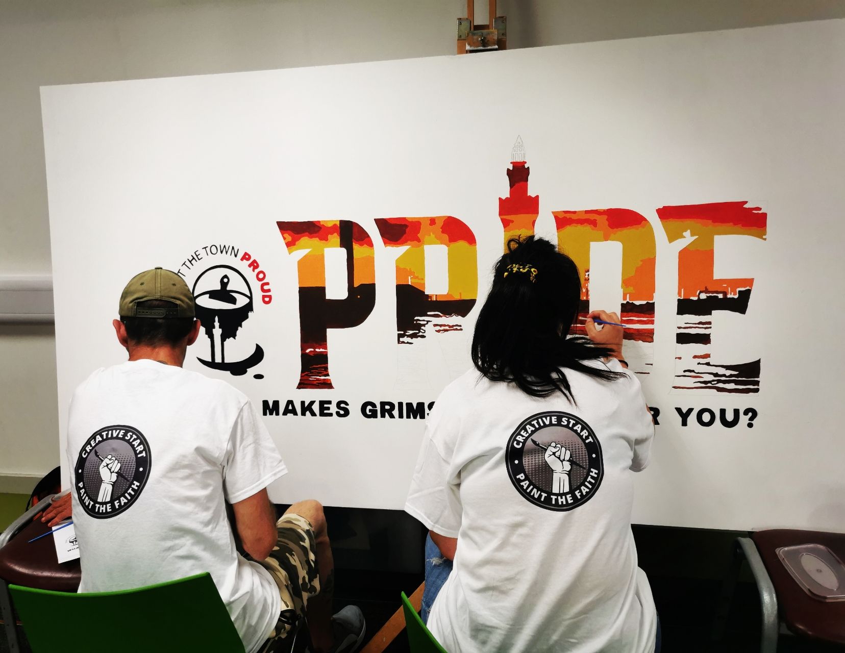 Two people are painting the word pride on a wall