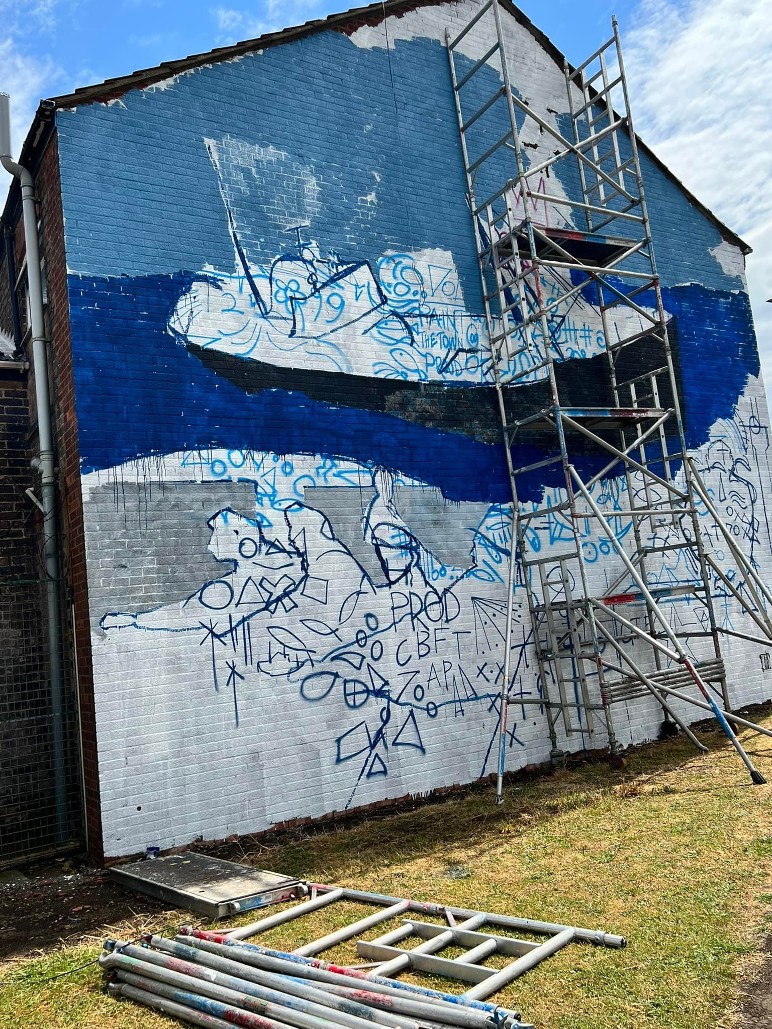 A large mural is being painted on the side of a building.
